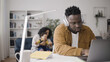 © Synthex - African American man working on laptop in headphones while mother is trying to comfort crying baby