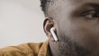 © Synthex - Close-up of African American man with wireless earbuds in his ears, testing new device