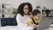 © Synthex - Young black mother works from home and takes care of her baby, earning extra income