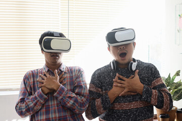 Two young Asian men showing shocked expression when playing game using virtual reality headset.  Modern technology concept