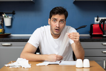 Wall Mural - Close up of unhappy man sitting at the table, stressed and confused by calculate expense from invoice or bills, have no money to pay mortgage or loan. High prices and spending money concept