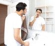 © Vitaliy - Handsome man looking at the mirror and shaving in the bathroom