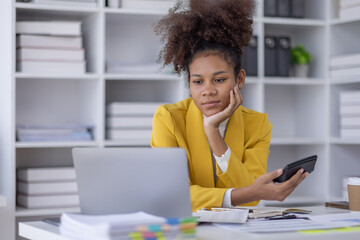 Wall Mural - Young business african american woman office worker analyst sitting at desk working on laptop thinking on project plan, analyzing marketing or financial data online, watching elearning webinar.