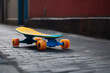 Blue skateboard with yellow and orange wheels on concrete tiles in an alley