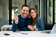 © bnenin - A smiling business couple in love sitting at the office table and using a credit card.