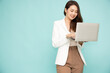© comzeal - Asian business woman in suit holding a laptop while standing isolated on green background