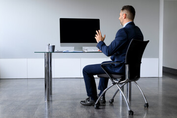 Rear view of middle aged businessman looking at blank empty computer monitor, having online web video call in office