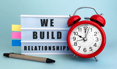 Poster - Text we build relationships written on the lightbox with alarm clock and colorfull stickers on blue background