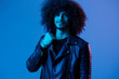 Portrait of fashion man with curly hair on blue background multinational, colored light, black leather jacket trend, modern concept.