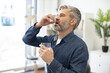 © sofiko14 - Caucasian middle-aged caucasian man taking pill and drinking glass of fresh water in doctor's office. Grey-bearded male person dressed in denim shirt following cardiologist's instructions.