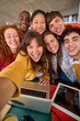 © CarlosBarquero - Vertical selfie with mobile phone of multiracial cheerful group of students gathered in hall of university building. Happy young friends hugging laughing and posing for photo. People smiling on campus