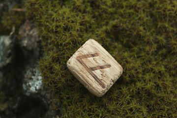 Wall Mural - Wooden rune Ansuz on stone with moss outdoors, closeup