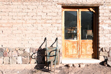 Frontal Rural Building With Adobe Brick Wall Entrance, Double Wooden Door With Crystal Pane And Light Blue Metal Wheelbarrow Stopped Leaning On The Warehouse Wall