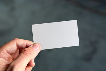 Hand Holding Blank White Card on Dark Grey Floor 
Background