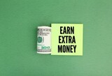 Fototapeta  - a roll of paper money and colored paper with the word earn extra money. the concept of earning extra money. the concept of extra money. Concept of financial planning Make more extra money 