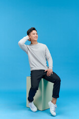 Wall Mural - Casual young man sitting on a mint column isolated on blue background