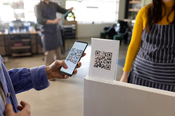Midsection of caucasian female client scanning qr code with smartphone at hair salon