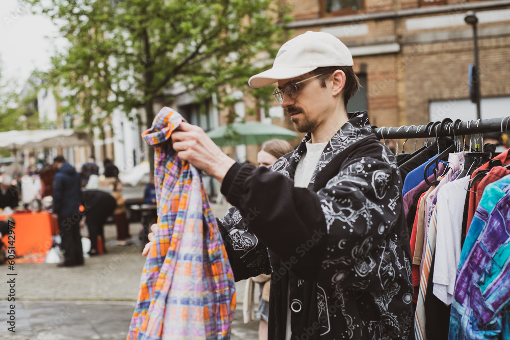 man with cap folds second hand clothes for sale at street market