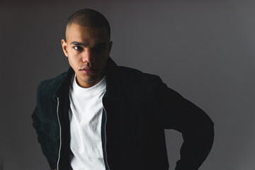 Wall Mural - young and handsome Afro-American man with white T-shirt and black jacket on the grey background, medium shot. High quality photo