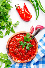 Spicy Tomato Pepper Sauce With Hot Chili Peppers, Garlic And Herbs On White Kitchen Table Background, Top View