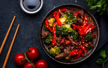 Stir Fry Vegetables With Sliced Beef, Red Paprika And Broccoli With Sesame Seeds In Ceramic Bowl On Black Table  Background, Top View