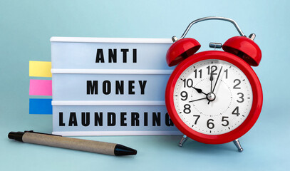 Poster - text anti money laundering written on the lightbox with alarm clock and colorfull stickers on blue b