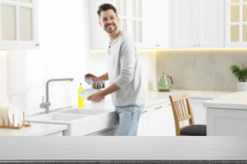 Wall Mural - Man doing washing up in kitchen, focus on empty grey stone table