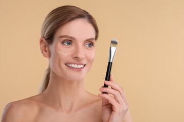 Wall Mural - Woman with swatch of foundation holding makeup brush on beige background. Space for text