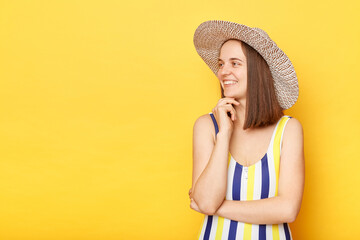 Dreamy positive optimistic woman wearing striped swimming suit and hat isolated on yellow background looking away with smile copy space for advertisement.
