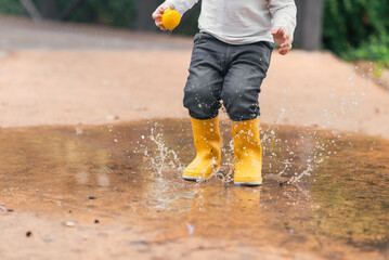 Child's feet in yellow rubber boots jumping over a puddle in the rain