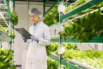 Aufkleber - Young female scientist in lab coat looking through document while learning information about new sorts of lettuce in greenhouse