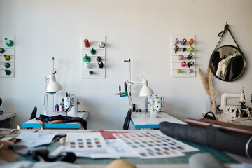 Poster - Focus on workplaces of seamstresses or tanners with electric equipment, lamps and colorful spools of threads on the wall in workshop