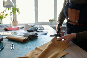 Aufkleber - Close-up of female leatherworker in apron cutting leather or suede while standing by table in front of camera and creating new attire