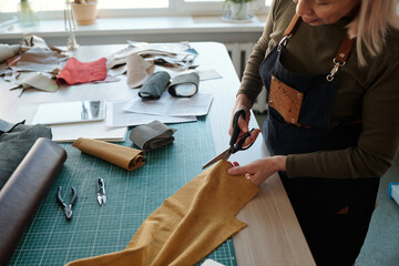 Aufkleber - Cropped shot of mature female leatherworker cutting piece of suede or leather with scissors while working over new creative apparel