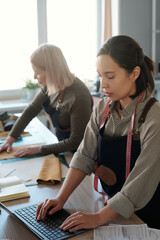 Aufkleber - Focus on young brunette female leatherworker typing on laptop keyboard while checking online orders of clients against mature colleague