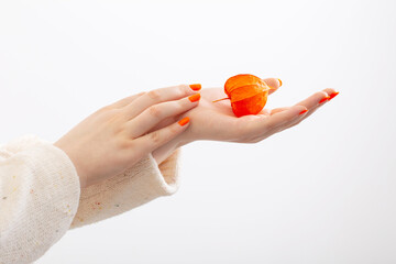 female hand with orange manicure with physalis on white background