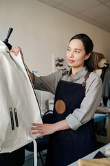 Aufkleber - Young pretty tailor standing in front of mannequin with new white leather jacket while working over client order of fashion collection
