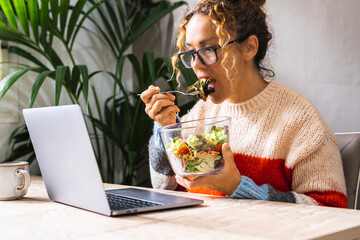 Woman busy working on laptop and eating a salads at the same time. Fast lunch break for online job activity. Concept of diet and modern work. Casual female in telecommuting smart working life alone