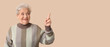 © Pixel-Shot - Senior woman pointing at something on beige background with space for text