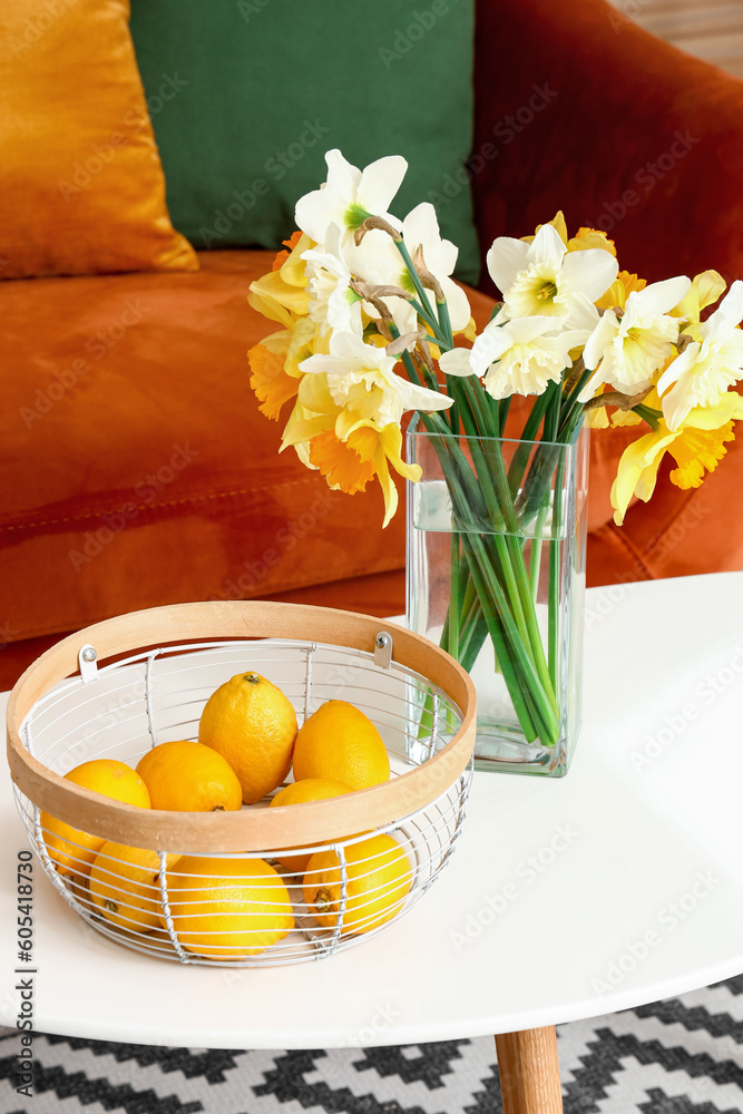 Vase with narcissus flowers and lemons in basket on coffee table