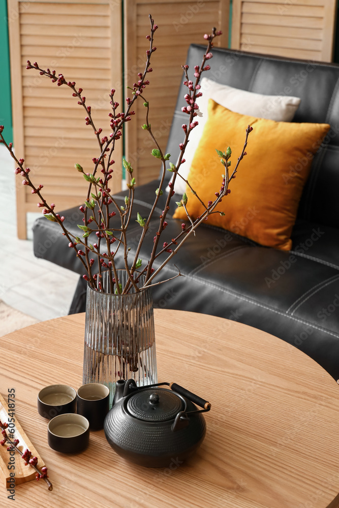 Vase with blooming tree branches and tea set on table in living room