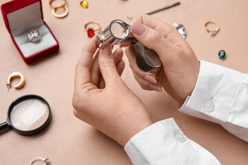 Female jeweler examining ring on beige table, closeup