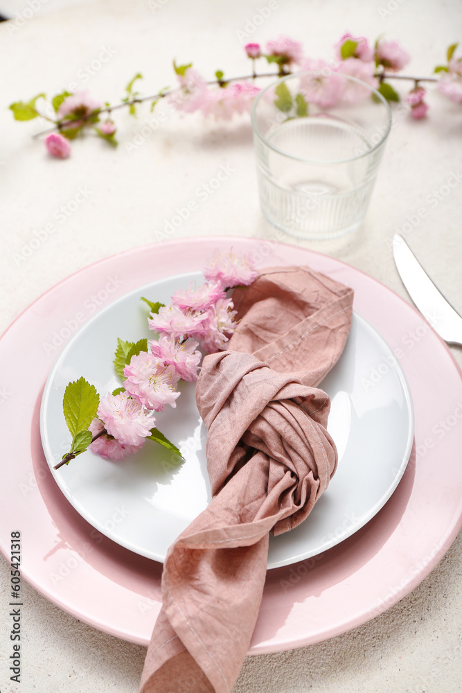 Beautiful table serving with cutlery, blooming tree branches and folded napkin on white grunge background