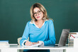 © Volodymyr - Female teacher. Sensual student woman in eyeglasses near blackboard. Sexy girl sit on table on chalkboard. Attractive female teacher in college.