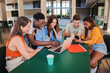 © Jose Calsina - Multiracial smiling group of friends, high school students using laptop to search information on internet, sitting at library. Young teenage people using devices studying for a university project