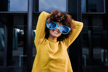 Wall Mural - young afro american woman wearing vibrant sunglasses in city of Latin America, Hispanic and caribbean female with afro hair for party carnival 