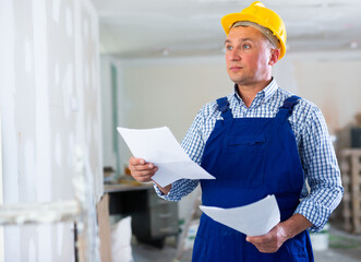 Wall Mural - Portrait of foreman with documentation in apartment during repair works. Builder in overall and hardhat checking project documentation.