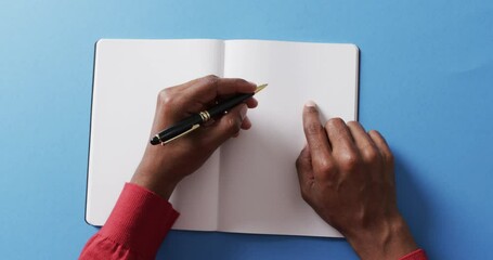 Wall Mural - Close up of hand writing with pen on book with copy space on blue background in slow motion