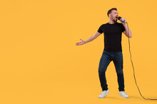 Handsome Man With Microphone Singing On Yellow Background. Space For Text