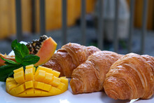 Three Appetizing Fresh Croissants On A White Plate Outdoors In Restaurant Papaya Mint Mango Tropical Fruit Serving Desserts After Baking Restaurant Shop Serving Holiday About Creating Atmosphere